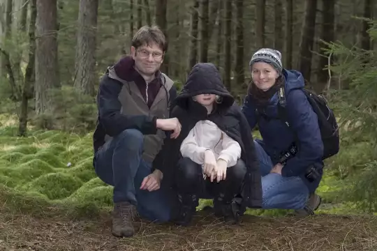 Drei Personen knieend im Wald vor großen Moospolstern einer Flußniederung