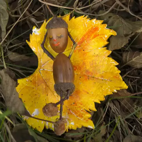 Eine aus einer Eichel gebastelte Gestalt liegt auf einem gelben Blatt