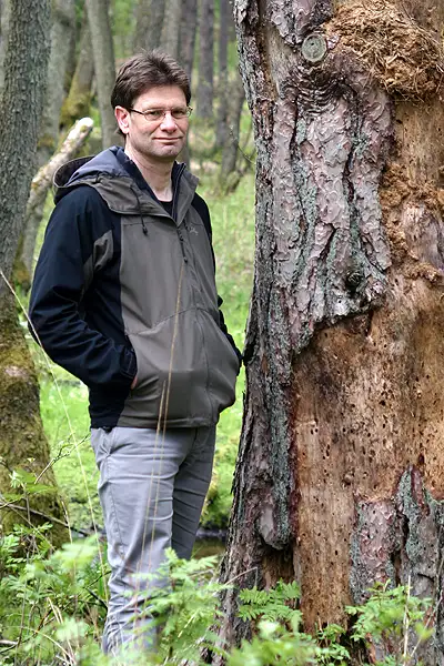 Jürgen Eggers Ein Mann steht neben einer toten Kiefer, deren Borke am Stamm teilweise abgefallen ist