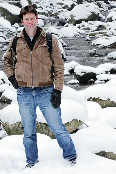 Ein Mann steht in einer verschneiten Winterlandschaft vor einem Gebirgsbach