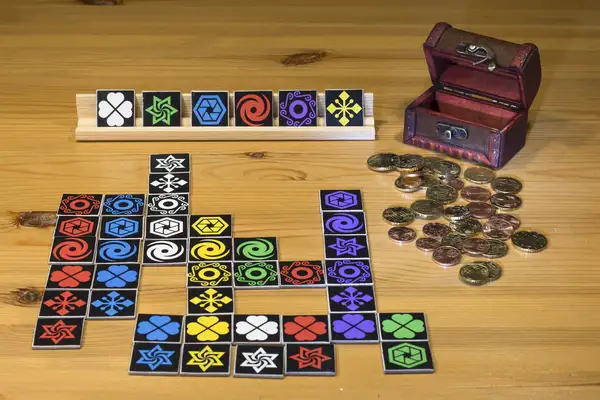 Legespiel Twirkle Quadratische Karten mit verschiedenen Symbolen und Farben und Euromünzen auf einem Holztisch